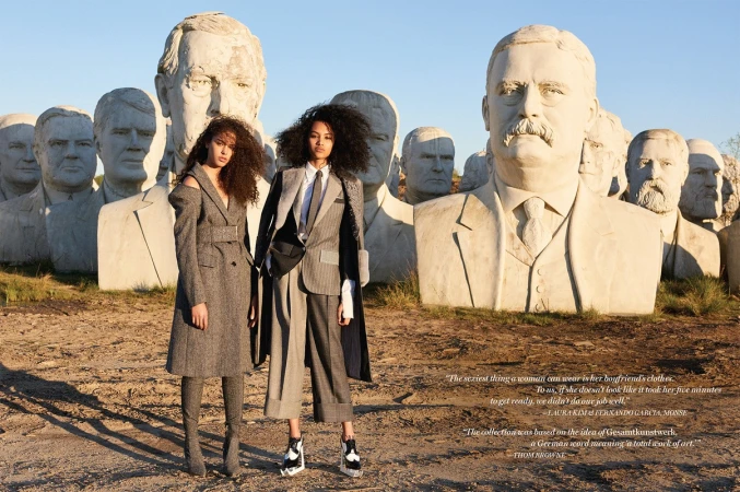 Two female models posing outdoors in front of giant presidential bust sculptures with warm sunlight.