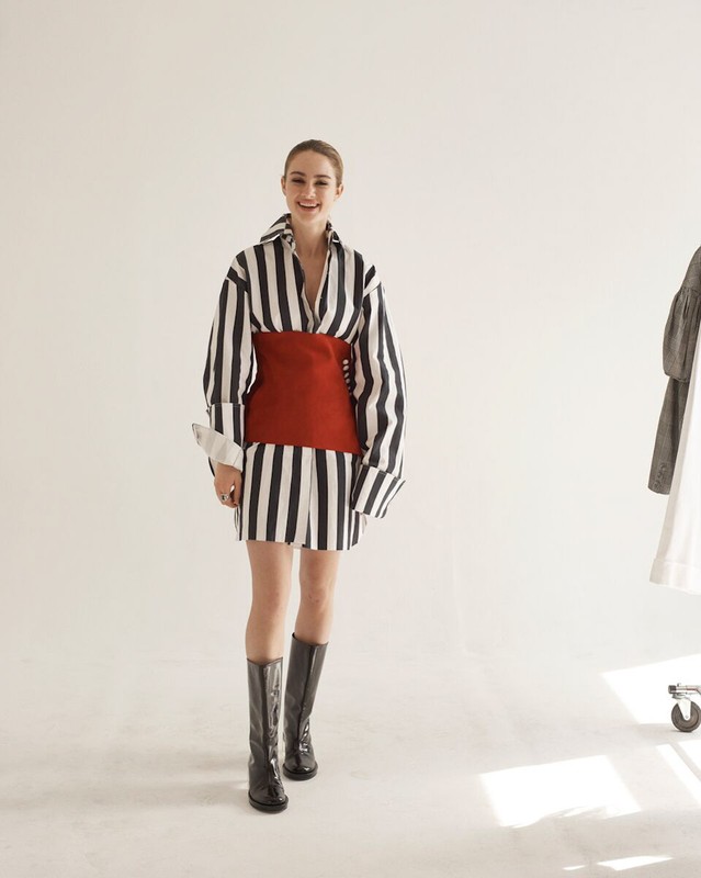 Model in vertical striped shirt dress with a red waist wrap and black boots in a studio setting