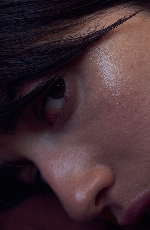 Close-up portrait of a woman's face highlighting natural skin texture and dark hair framing her eye and cheek.