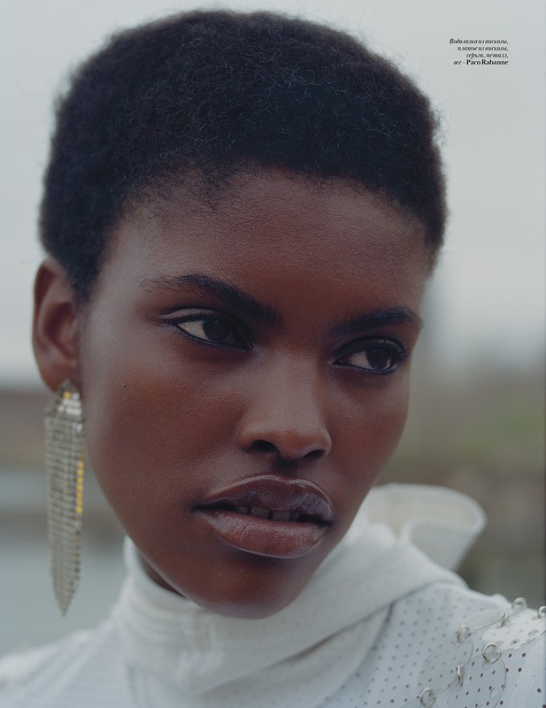 Close-up portrait of a Black woman with short hair wearing a white high-neck garment and silver earrings