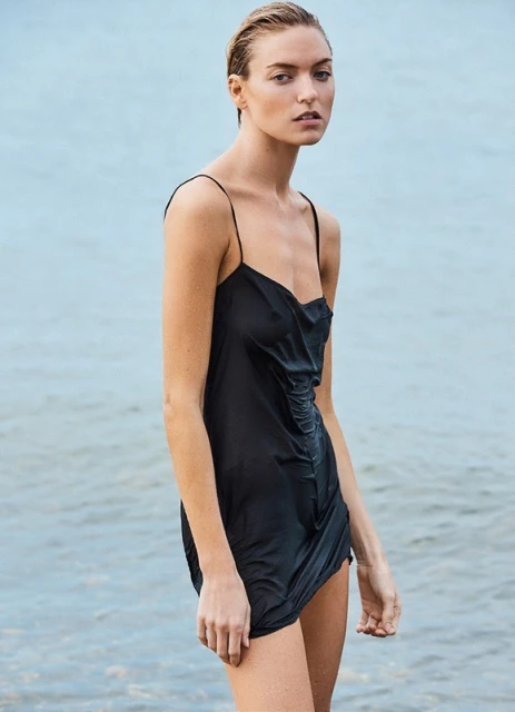 Woman in a wet black dress poses standing in water. The lighting is soft. The scene is a close-up, portrait orientation.