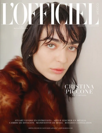 Magazine cover portrait of a dark-haired woman wearing a rust-colored fur coat against a plain wall.