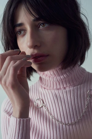 Close-up portrait of a woman with dark bob hair wearing a ribbed pink turtleneck with silver chain hardware by make-up artist Campbell Ritchie