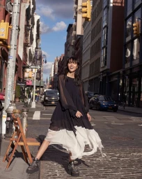 Model in a black and white pleated dress and platform boots posing on a city street with traffic and buildings