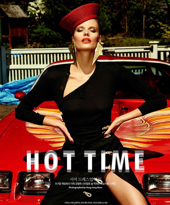 Fashion editorial shot of a Caucasian woman in a black outfit and red hat, posing against a red vintage car in an outdoor setting.