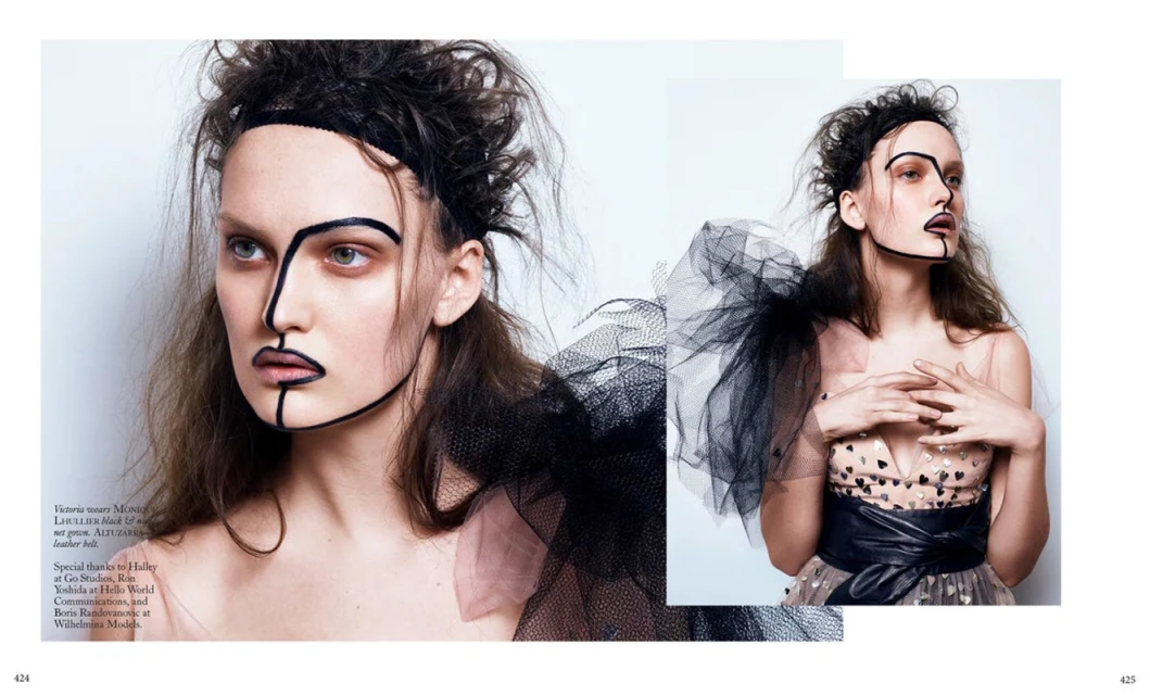 Editorial fashion shot featuring a woman with graphic face makeup, tulle accent, wearing a heart-print dress with a wide leather belt.