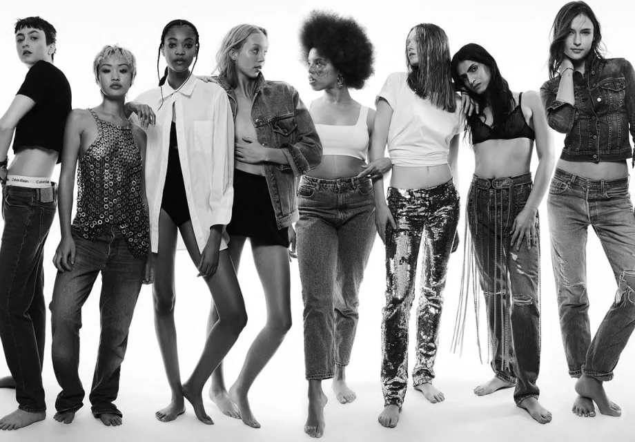 Group of diverse women in denim and crop tops posing in a studio setting, showcasing fashion and body positivity, set against a white backdrop.