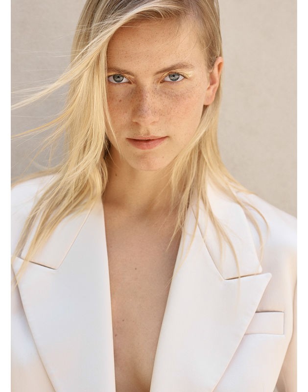 Portrait of a blonde woman with freckles wearing a white blazer against a neutral backdrop