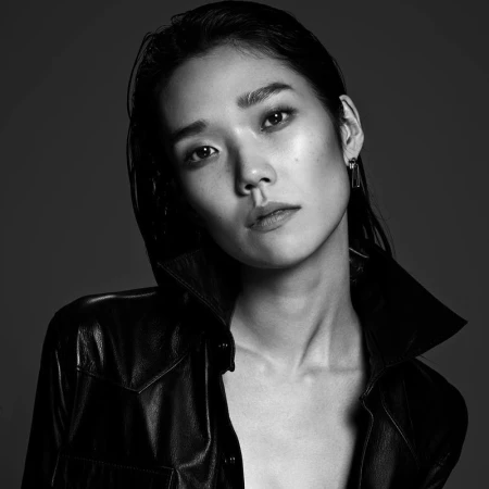 Close-up monochrome portrait of an East Asian woman with wet-look hair wearing a dark leather shirt.