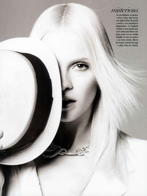 Monochrome portrait of a model with platinum blonde hair, wearing a Chanel necklace, partially obscured by a wide-brimmed hat.