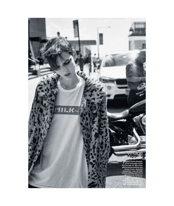 Monochrome fashion shot of a person in a white tee shirt and leopard print jacket standing next to a motorcycle on a city street.