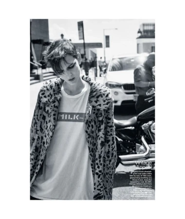 Monochrome fashion shot of a person in a white tee shirt and leopard print jacket standing next to a motorcycle on a city street.