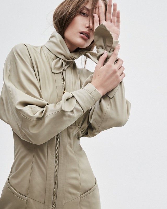 Portrait of an adult woman with light skin, wearing a black turtleneck, posing in a photo studio with a grey background.
