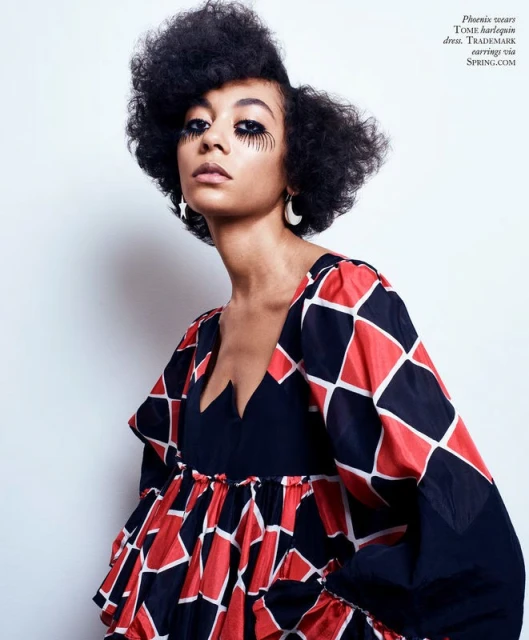 Portrait of a young African-descent woman with big dark hair, wearing a harlequin dress with dramatic eye makeup, shot in a studio.