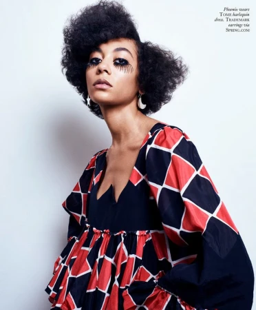 Portrait of a young African-descent woman with big dark hair, wearing a harlequin dress with dramatic eye makeup, shot in a studio.