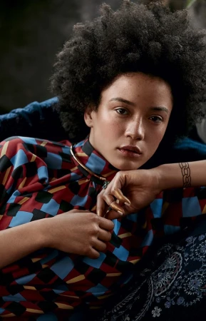 Portrait of a woman with curly dark hair and patterned top resting chin on hands by set designer Chelsea Maruskin