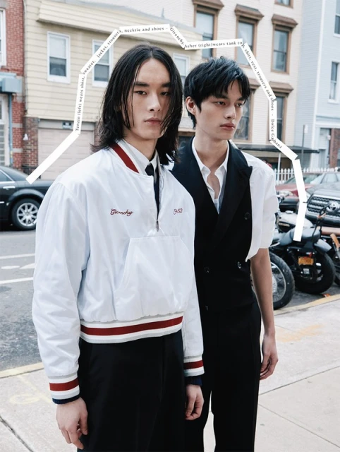 Two Asian male fashion models pose in urban street setting wearing stylish outerwear, vests, and trousers next to motorcycles.
