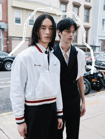 Two Asian male fashion models pose in urban street setting wearing stylish outerwear, vests, and trousers next to motorcycles.