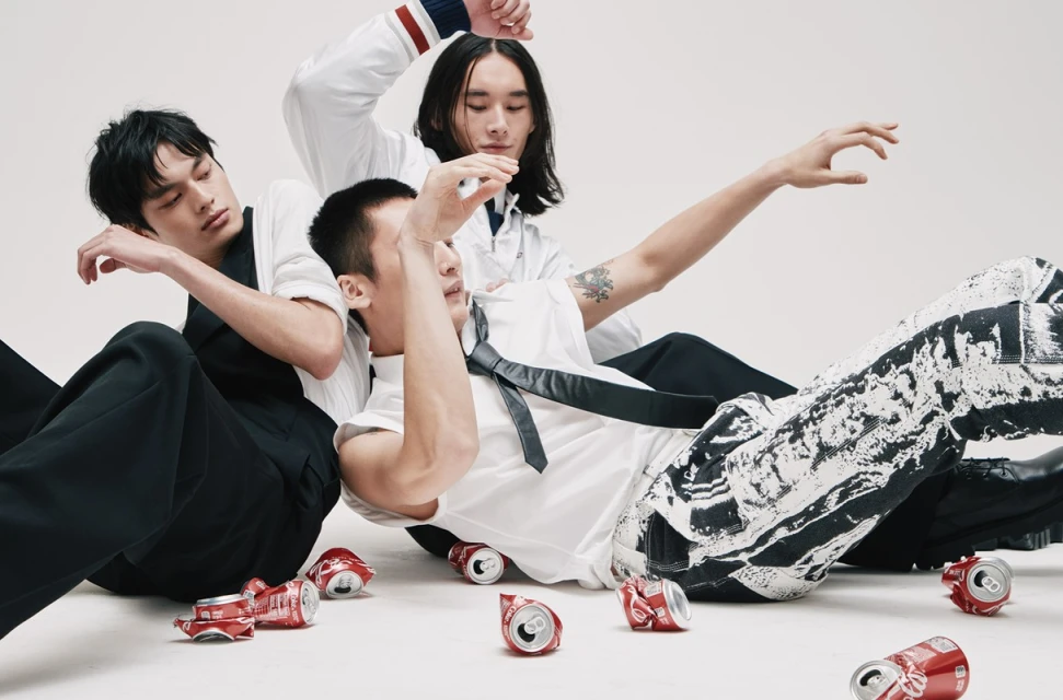 Three Asian males pose with crushed beverage cans in a bright indoor studio setting. Fashion photography with modern style.