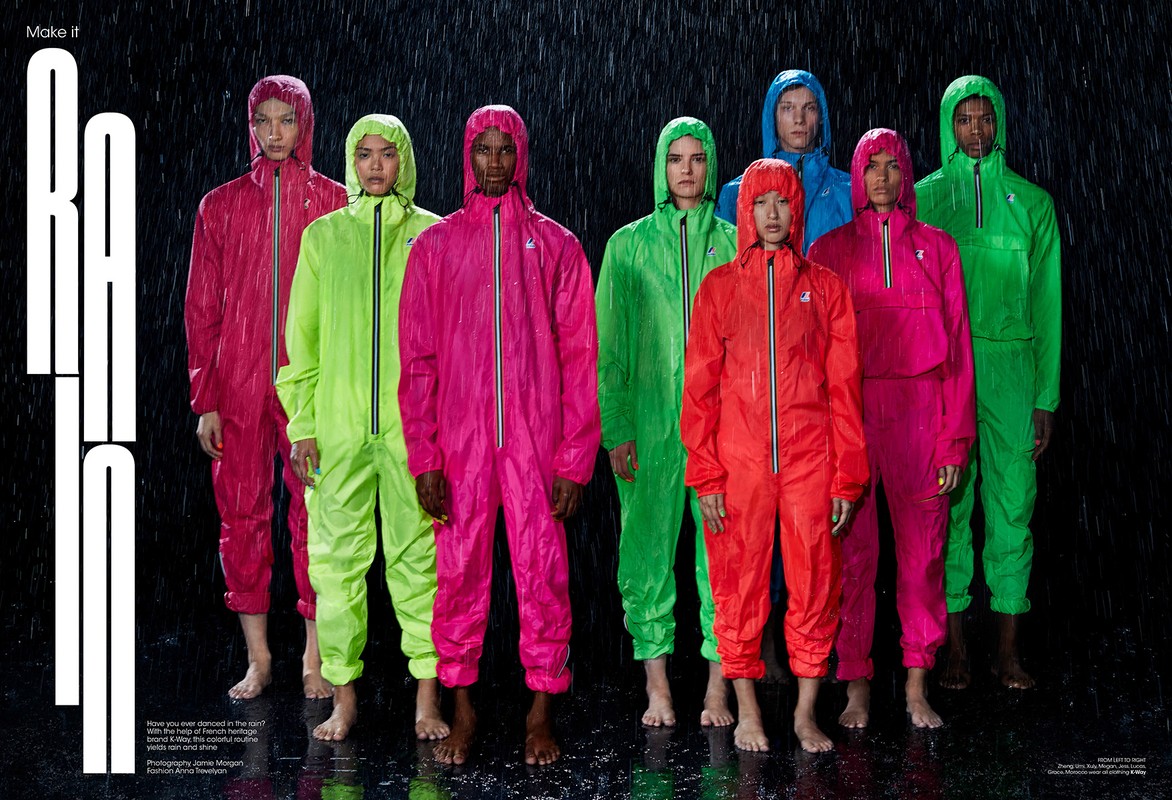 Group of diverse adult models in colorful hooded jumpsuits standing barefoot in the rain against a black background for a fashion editorial.