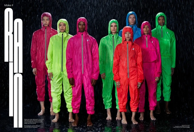 Group of diverse adult models in colorful hooded jumpsuits standing barefoot in the rain against a black background for a fashion editorial.