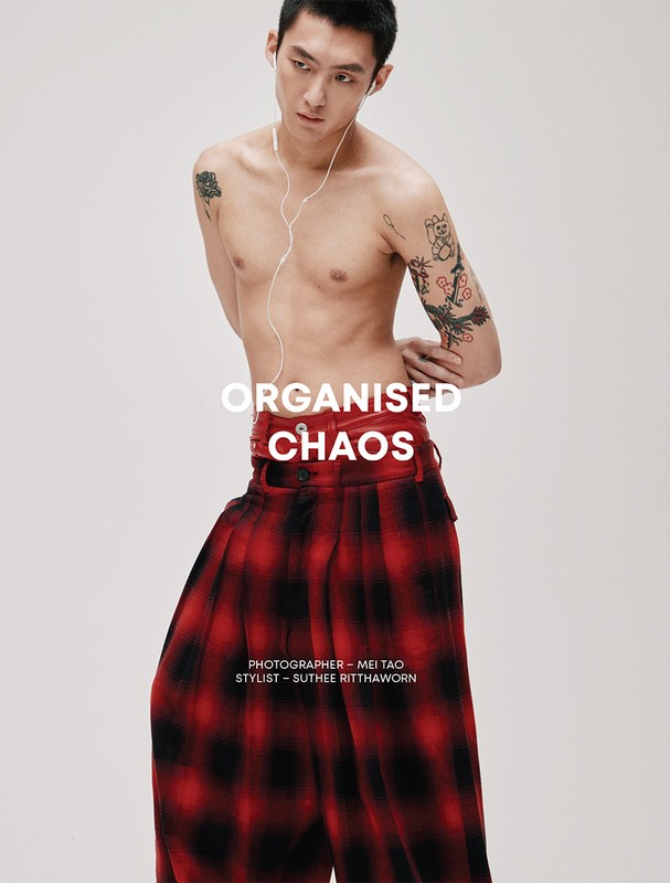 Shirtless man in studio with tartan pants, listening to earbuds, against a white backdrop with graphic designer and stylist credit.