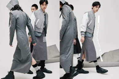 Group of male models wearing grey coats, jackets, and skirts against a plain white background with grey fabric pieces.