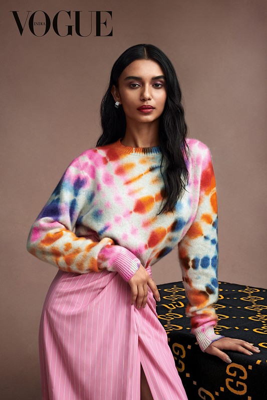 A captivating portrait of an adult woman with dark hair in a colorful tie-dye sweater and pink skirt, posing in a studio for Vogue.