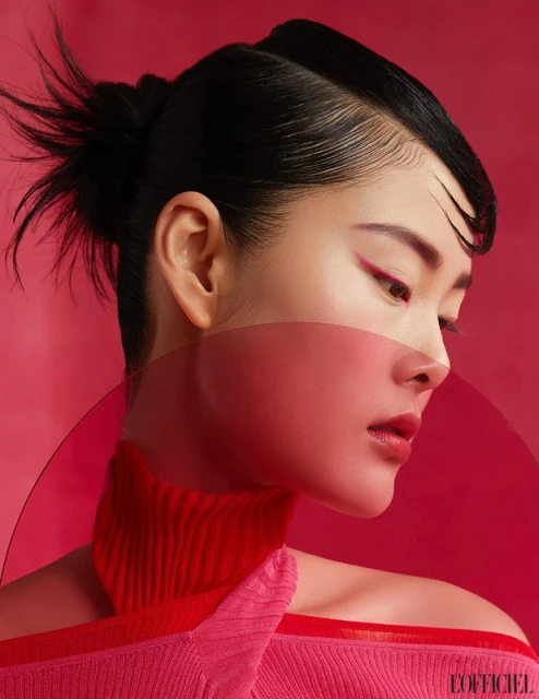 Asian woman in red-themed beauty portrait, featuring stylish hair, makeup, and a translucent panel in a minimalist studio setting.