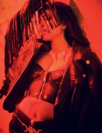 Woman in black leather jacket and bustier with red fringe hair piece under dramatic red lighting
