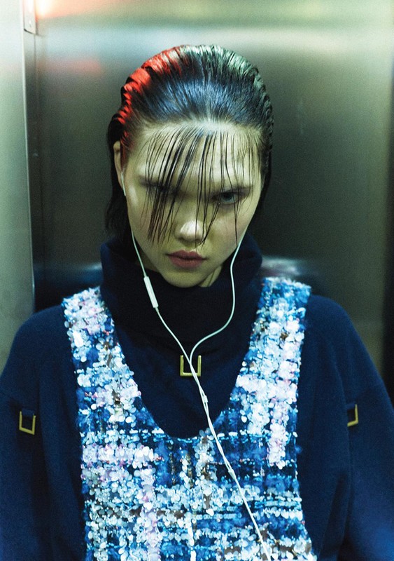Close-up shot of a stylish young adult female with wet slicked-back hair and bangs, wearing a navy blue top with a tweed vest.