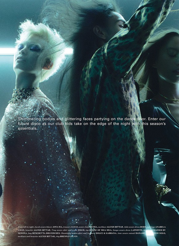 Editorial fashion shot of three people with unique hairstyles wearing shiny, textured clothing in an indoor setting with blue lighting.