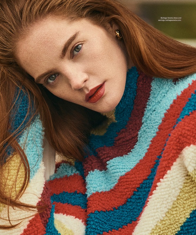 Close-up portrait of a red-haired woman wearing a colorful striped textured sweater with gold earrings by make-up artist Chichi Saito.