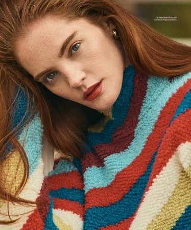 Close-up portrait of a red-haired woman wearing a colorful striped textured sweater with gold earrings by make-up artist Chichi Saito.