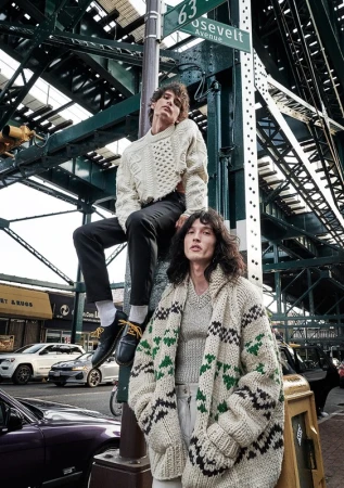 Two adult males showcasing knitwear fashion in an urban outdoor setting with cars, street signs, and elevated train tracks.