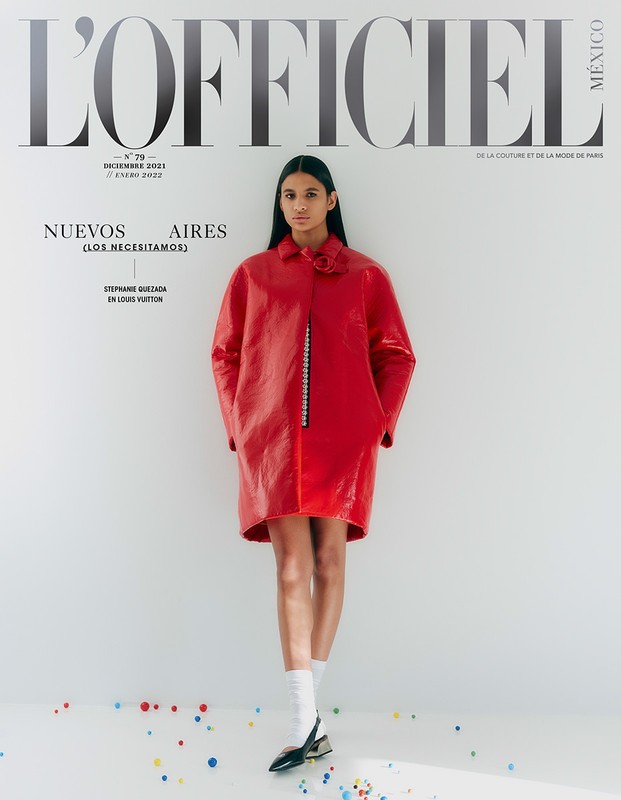 Fashion editorial cover with a woman in a red vinyl coat, white socks, and black heels standing in a white studio with colorful confetti.
