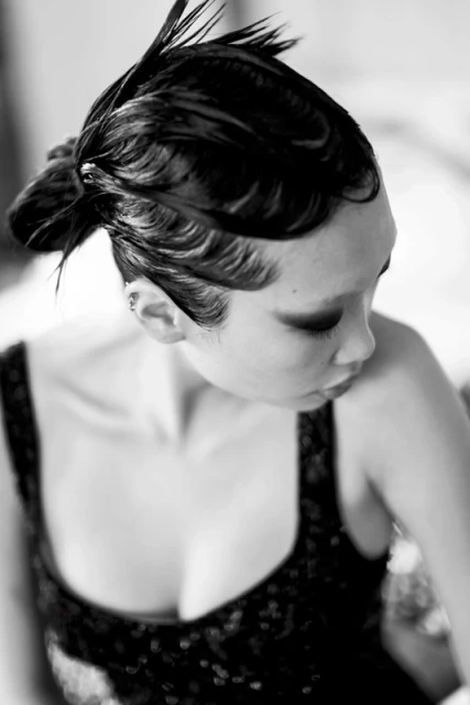 Black and white portrait of an Asian woman with dark hair styled with finger waves, wearing a black sleeveless top.  Looking down.