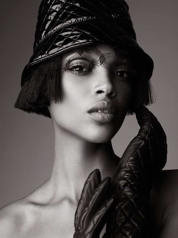 Glamorous portrait of an adult woman in black bucket hat and gloves, set against a soft gray background. Fashion and beauty concept.