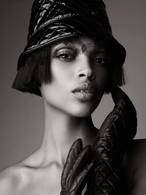 Glamorous portrait of an adult woman in black bucket hat and gloves, set against a soft gray background. Fashion and beauty concept.