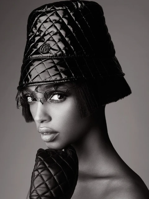 Close-up fashion portrait of a woman wearing a quilted hat and gloves against a neutral background in black and white.