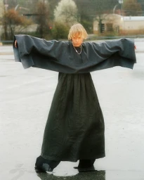 Model with blonde bob wearing dark grey wide-sleeved garment and long skirt outdoors in Los Angeles with makeup by Chichi Saito