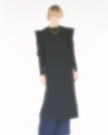 Model with blonde bob wearing a black long-sleeved dress against a bright white blurred background