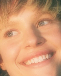 Close-up portrait of a smiling woman with light blonde hair and blue eyes, featuring makeup by Chichi Saito in Los Angeles.