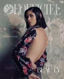 Editorial cover featuring a woman with dark bobbed hair wearing a patterned open-back top against a textured wall.