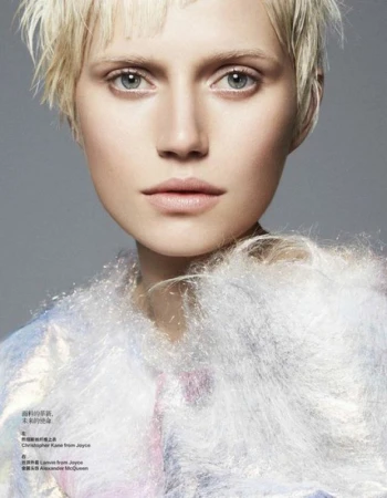 Close-up portrait of a woman with short blonde hair and light blue eyes wearing a textured white garment.