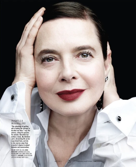 Portrait of Isabella Rossellini with hands near her face wearing a white collared shirt against a dark background in a magazine spread.