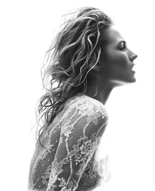 Black-and-white portrait of an adult woman in a lace top looking right, featuring blonde hair, studio lighting, and a clean, white background.