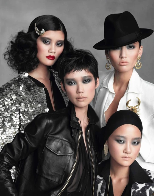 Four Asian women in diverse fashion styles pose in a studio portrait with black and white outfits and dramatic makeup against a grey background.