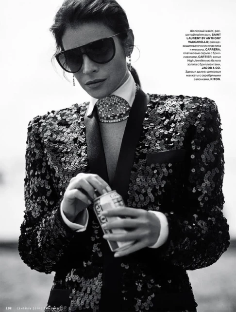 Fashion shot of a woman in a sequined blazer and sunglasses, holding a can. Black and white image with a shallow depth of field.