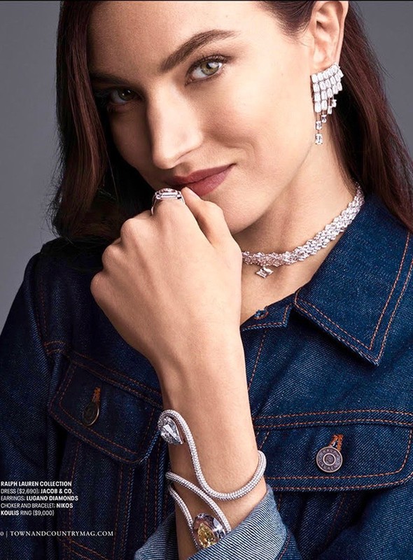 Close-up of a woman wearing a blue denim jacket and sparkling jewellery, including earrings, a necklace, a ring and a bracelet.